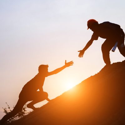 Tourists go up the hill in the sunrise. Tourists go up the hill in the sunrise to shake hands The male traveler shakes the hand of the male traveler who is climbing to the top of the hill
